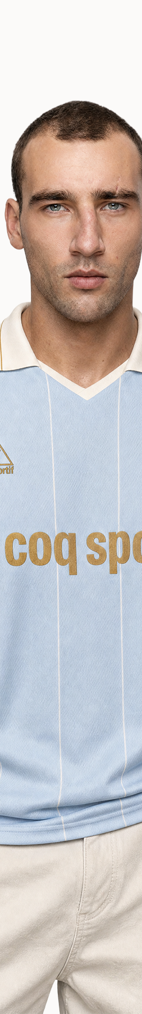 A man wearing a light blue Le Coq Sportif retro football jersey with cream sleeves