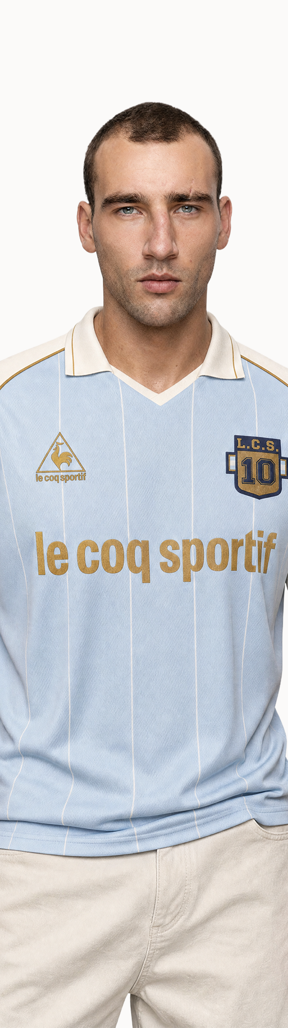 A man wearing a light blue Le Coq Sportif retro football jersey with cream sleeves