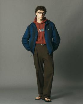 A man wearing a blue le PÈRE hooded jacket over a rust graphic hoodie with brown trousers