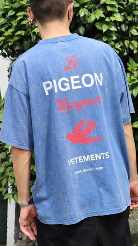 A man wearing a washed blue Le Pigeon Voyageur T-shirt with red pigeon back print