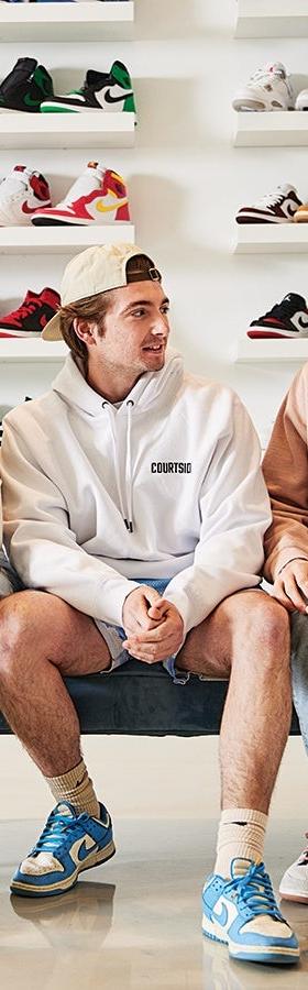Three men in hoodies and sneakers sitting in a sneaker boutique lined with shelves of Nike and Air Jordan shoes