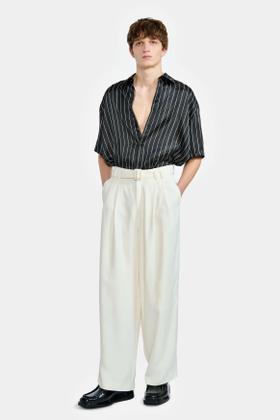 A man wearing a black pinstripe short-sleeve shirt and cream wide-leg trousers by LGN Louis Gabriel Nouchi