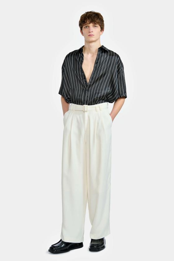 A man wearing a black pinstripe short-sleeve shirt and cream wide-leg trousers by LGN Louis Gabriel Nouchi