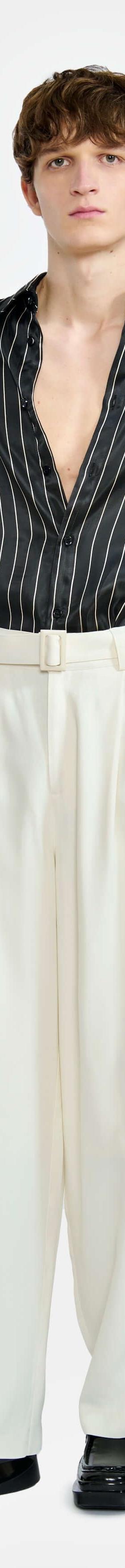 A man wearing a black pinstripe short-sleeve shirt and cream wide-leg trousers by LGN Louis Gabriel Nouchi