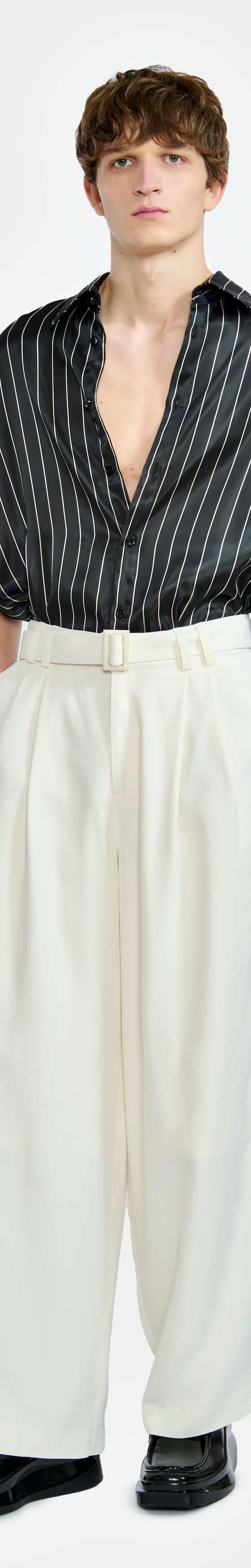 A man wearing a black pinstripe short-sleeve shirt and cream wide-leg trousers by LGN Louis Gabriel Nouchi