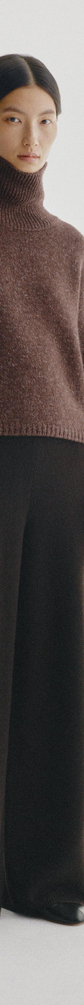 A woman wearing a brown cashmere turtleneck sweater and black wide-leg knit trousers