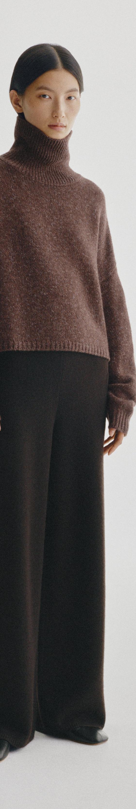 A woman wearing a brown cashmere turtleneck sweater and black wide-leg knit trousers