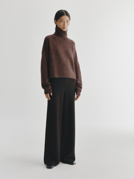 A woman wearing a brown cashmere turtleneck sweater and black wide-leg knit trousers
