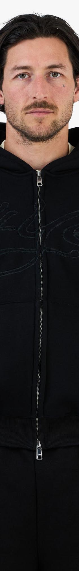 A man wearing a black zip-up hoodie and matching black sweatpants
