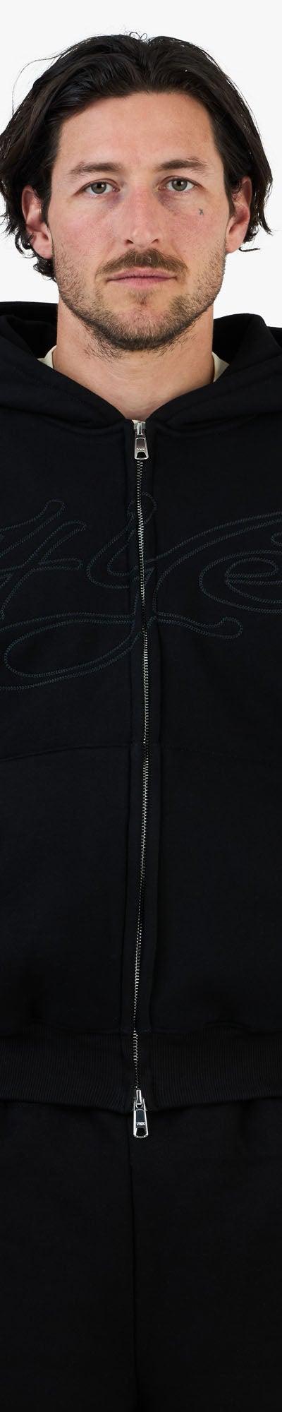 A man wearing a black zip-up hoodie and matching black sweatpants