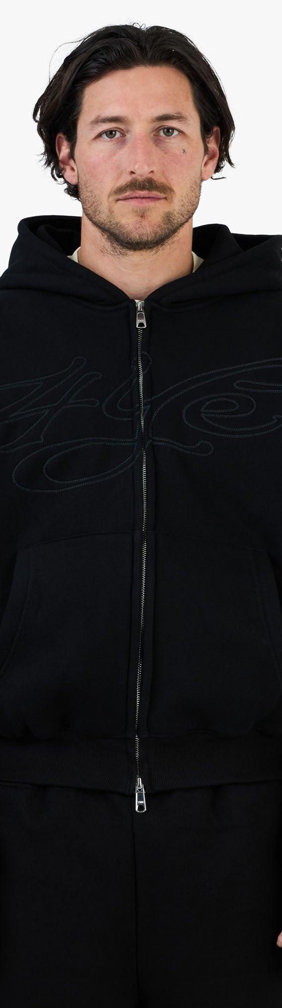 A man wearing a black zip-up hoodie and matching black sweatpants