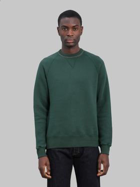 A man wearing a dark green Loop & Weft loopwheel raglan sweatshirt with indigo jeans