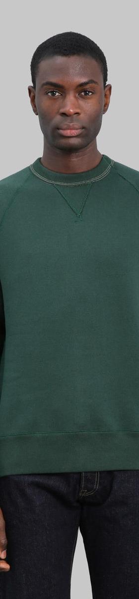A man wearing a dark green Loop & Weft loopwheel raglan sweatshirt with indigo jeans