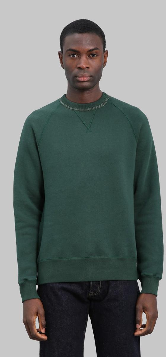 A man wearing a dark green Loop & Weft loopwheel raglan sweatshirt with indigo jeans