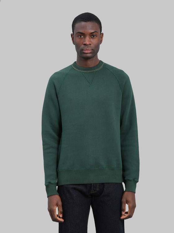 A man wearing a dark green Loop & Weft loopwheel raglan sweatshirt with indigo jeans