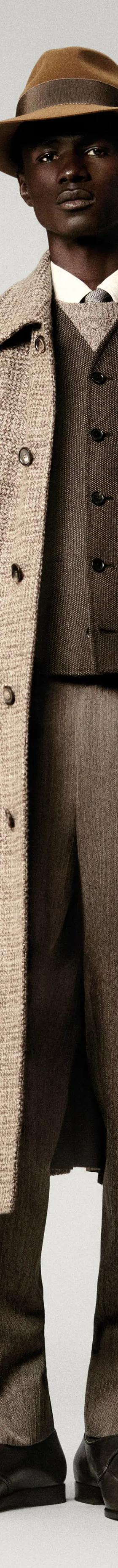 A man wearing a checked wool Loro Piana overcoat with matching tailored trousers and a felt hat