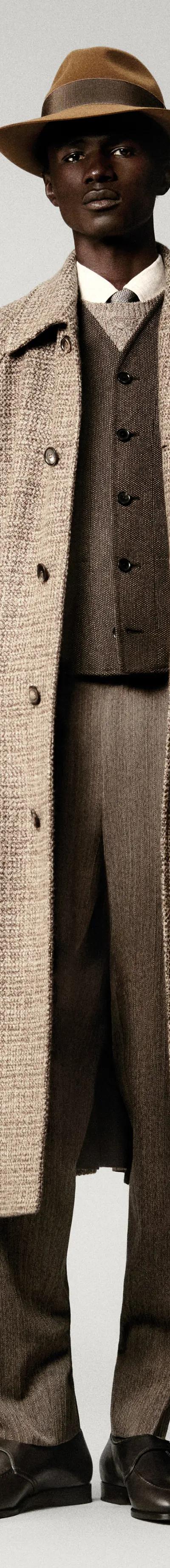 A man wearing a checked wool Loro Piana overcoat with matching tailored trousers and a felt hat