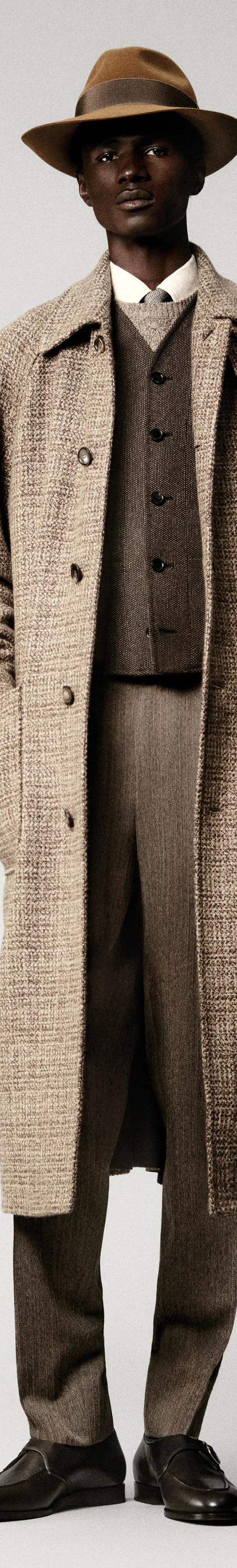A man wearing a checked wool Loro Piana overcoat with matching tailored trousers and a felt hat