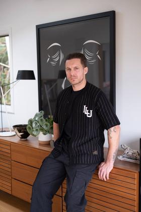 A man wearing a black pinstripe Lovely Disgraze short-sleeve shirt with black cargo trousers