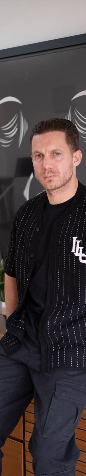 A man wearing a black pinstripe Lovely Disgraze short-sleeve shirt with black cargo trousers