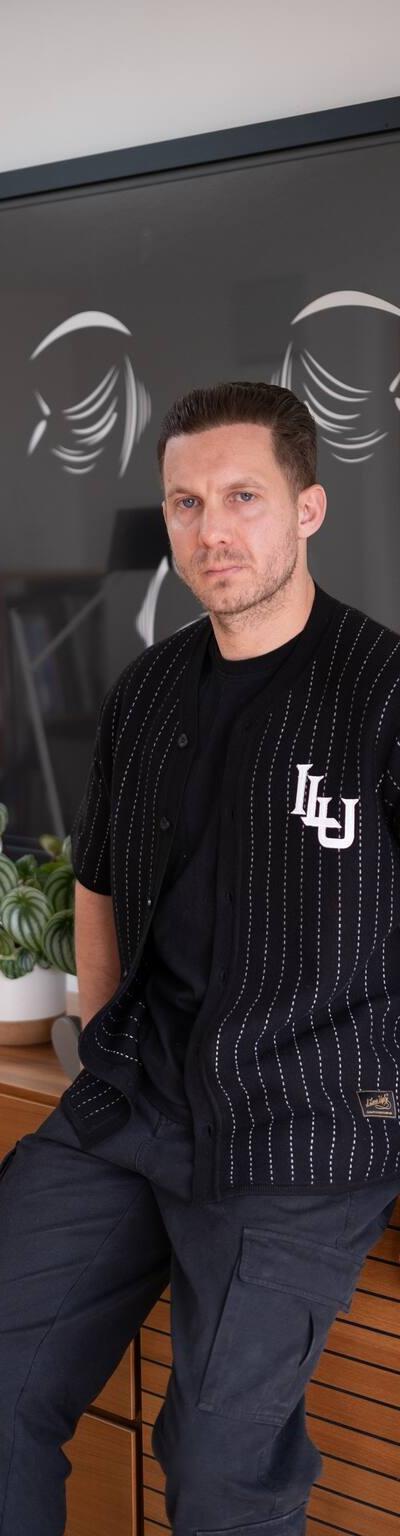 A man wearing a black pinstripe Lovely Disgraze short-sleeve shirt with black cargo trousers