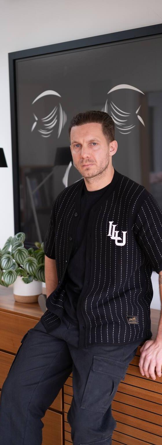 A man wearing a black pinstripe Lovely Disgraze short-sleeve shirt with black cargo trousers