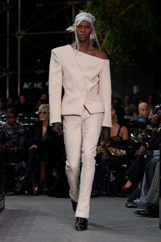 A model wearing a cream Luar asymmetric off-the-shoulder blazer and matching trousers on the runway