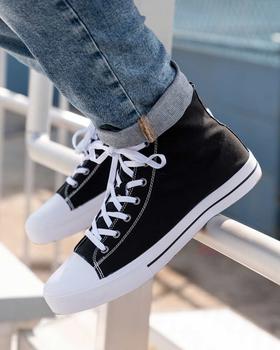 A person wearing black and white Lugz canvas high-top sneakers with cuffed jeans, feet resting on a railing