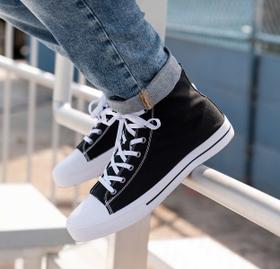A person wearing black and white Lugz canvas high-top sneakers with cuffed jeans, feet resting on a railing