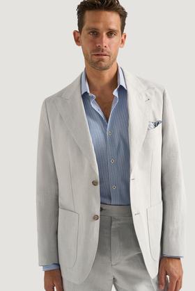 A man wearing a light grey M.J. Bale linen suit jacket with a blue striped shirt