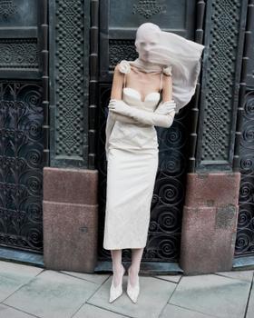 A woman wearing a cream strapless Magda Butrym midi dress with rosette detail, long gloves and a sheer veil