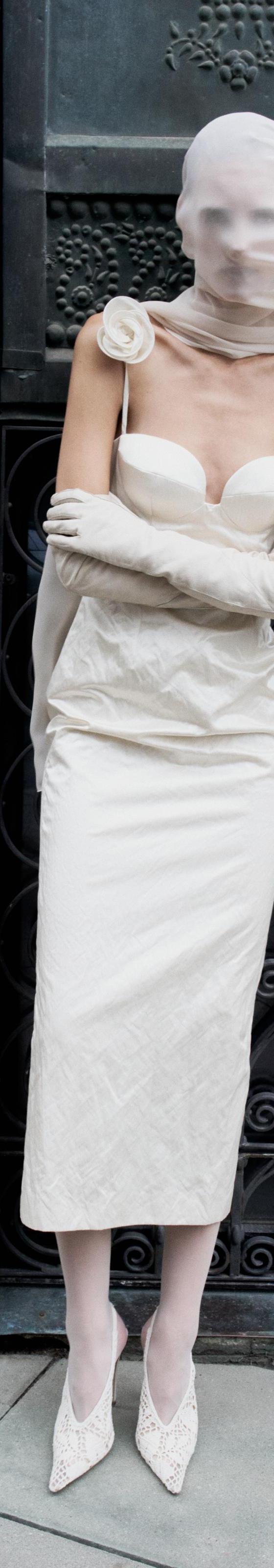 A woman wearing a cream strapless Magda Butrym midi dress with rosette detail, long gloves and a sheer veil