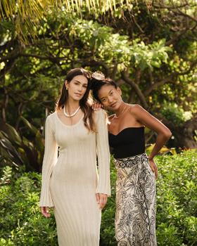 Two Mahina models in a knit dress and printed wrap skirt among palms