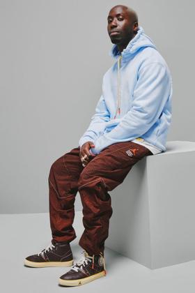 A man wearing a pale blue Maison Château Rouge hoodie with brown patterned trousers and high-top sneakers