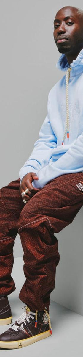 A man wearing a pale blue Maison Château Rouge hoodie with brown patterned trousers and high-top sneakers