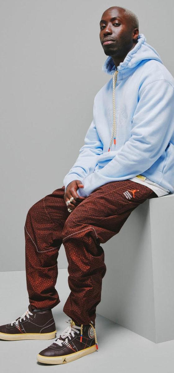 A man wearing a pale blue Maison Château Rouge hoodie with brown patterned trousers and high-top sneakers