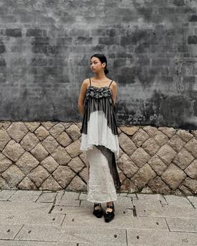 A woman wearing a ruched grey and ivory Maison Mume camisole top over a long white slip skirt