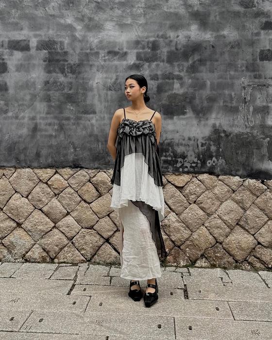A woman wearing a ruched grey and ivory Maison Mume camisole top over a long white slip skirt