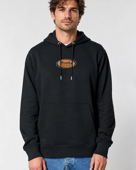 A man wearing a black Mambo hoodie with an orange Surf de Luxe oval logo
