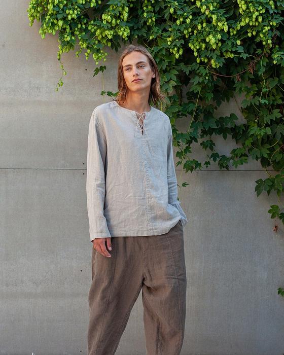 A man wearing a light linen pullover shirt and loose brown Manufacture de Lin linen trousers