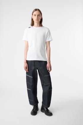 A man wearing a white Marithé + François Girbaud T-shirt and dark wide-leg cargo trousers