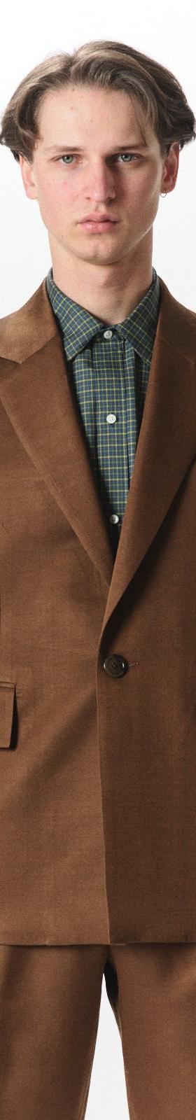 A man wearing a brown MARKAWARE tailored jacket over a green check shirt