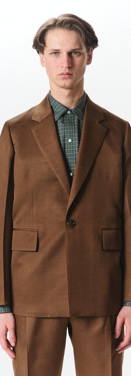 A man wearing a brown MARKAWARE tailored jacket over a green check shirt