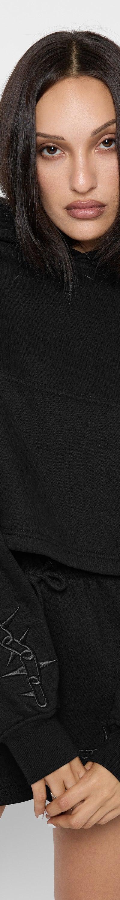 A woman wearing a black Mary Wyatt London cropped hoodie and matching shorts