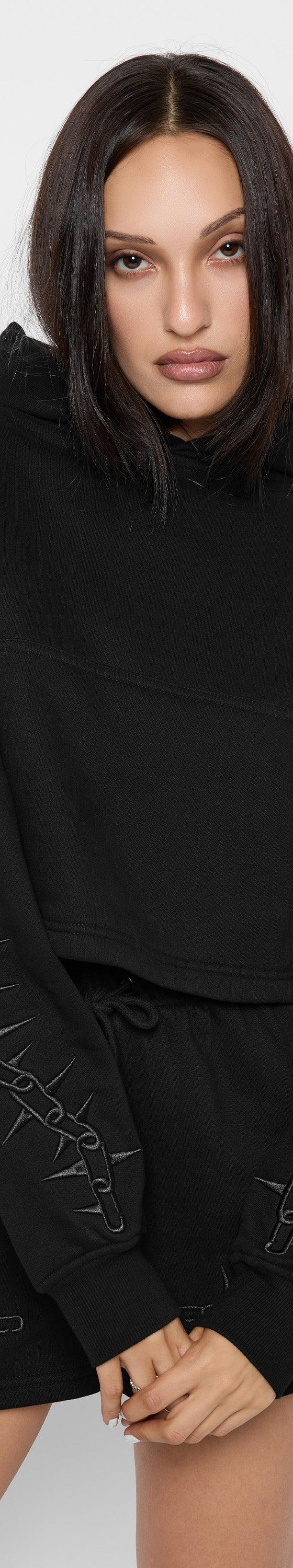 A woman wearing a black Mary Wyatt London cropped hoodie and matching shorts