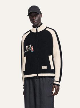 A man wearing a black and cream Mason Garments knit zip-up track jacket