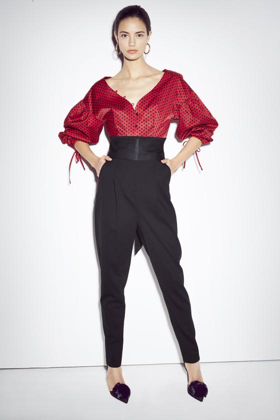 A woman wearing a red puff-sleeve blouse and high-waisted black trousers