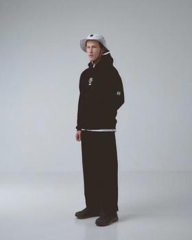A man wearing a black MECH hoodie with a globe logo, a white bucket hat and wide black trousers
