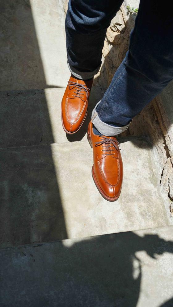 A man wearing tan leather Meermin derby shoes with cuffed dark denim