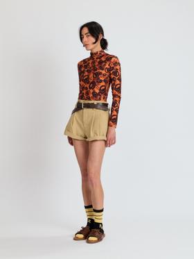 A woman wearing an orange printed Meryll Rogge turtleneck with khaki pleated shorts and brown sandals